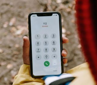 Close-up image of a hand dialing 112 emergency number on a smartphone outdoors.