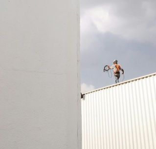 A construction worker stands on a rooftop against a large white wall, highlighting a minimalist aesthetic.